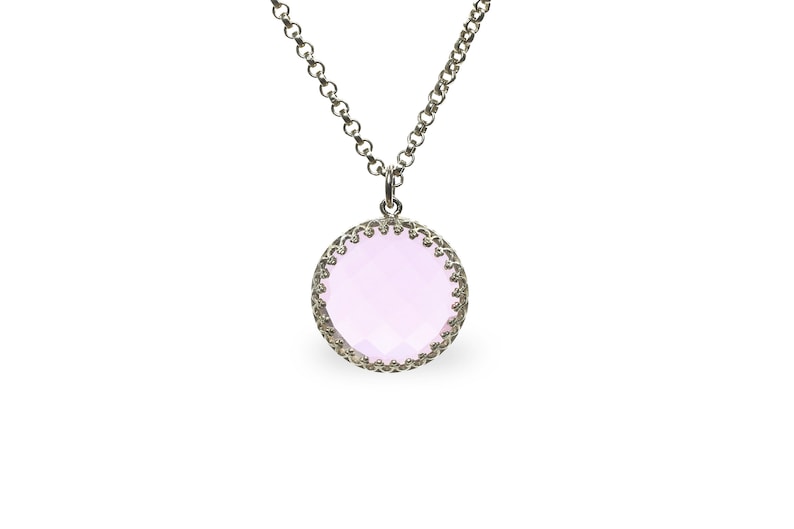 Op de afbeelding: Een zilveren ketting met een ronde hanger met een lichtroze edelsteen omgeven door een zilveren filigraanontwerp.