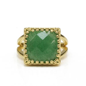 Puede incluir: Anillo dorado con una piedra preciosa verde cuadrada y facetada. La piedra preciosa est&aacute; engastada en un bisel decorativo y festoneado. El anillo tiene un dise&ntilde;o de ca&ntilde;a dividida, con dos bandas a cada lado de la piedra.