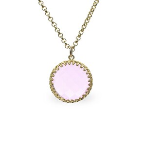 Op de afbeelding: Een gouden ketting met een roze edelsteen hanger. De hanger is rond en heeft een delicate gouden rand.