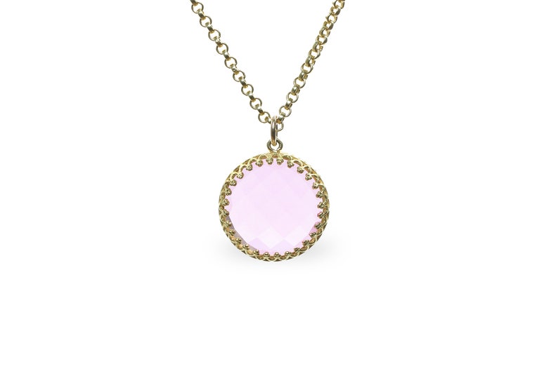 Op de afbeelding: Een gouden ketting met een roze edelsteen hanger. De hanger is rond en heeft een delicate gouden rand.