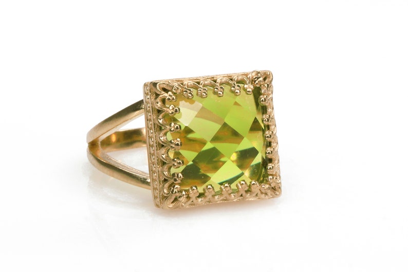 Puede incluir: Un anillo de oro con una piedra preciosa verde cuadrada engastada en un marco de oro decorativo.