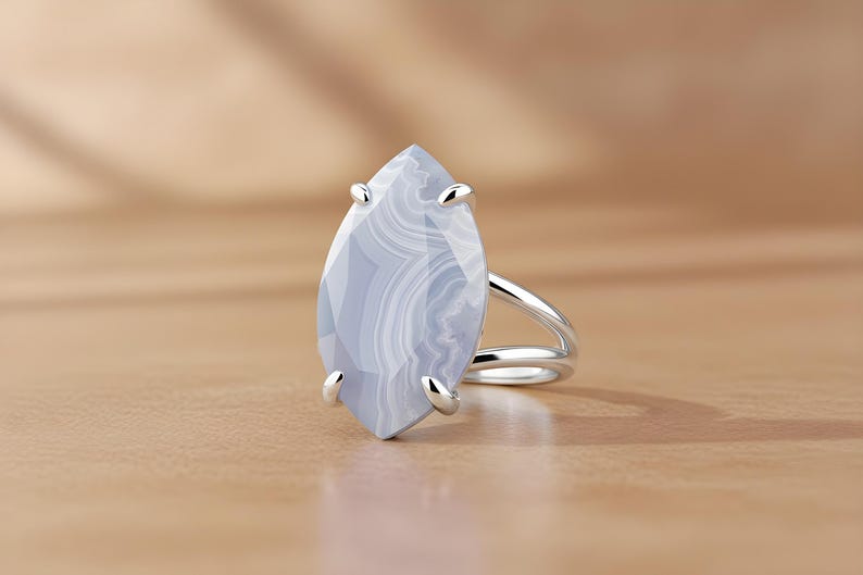 May include: A silver ring featuring a large, light blue gemstone with white marbling. The gemstone is marquise-shaped and held in place by four silver prongs. The ring has a split shank design.