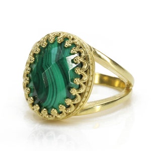May include: A gold ring featuring a large, oval-cut malachite stone with a vibrant green color and intricate veining. The ring has a split shank design and a decorative, openwork bezel setting.