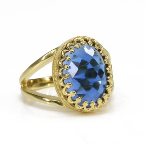 K&ouml;nnte beinhalten: Ein goldener Ring mit einem gro&szlig;en, facettierten, blauen Edelstein, der in einer dekorativen, goldenen Filigranfassung sitzt.