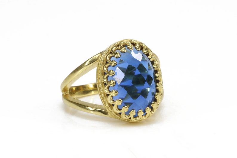 K&ouml;nnte beinhalten: Ein goldener Ring mit einem gro&szlig;en, facettierten, blauen Edelstein, der in einer dekorativen, goldenen Filigranfassung sitzt.
