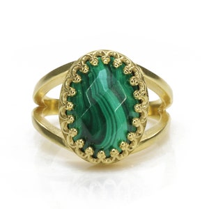 May include: A gold-colored ring featuring a large, oval-shaped malachite stone with a striking green and black pattern. The stone is set in a decorative, scalloped bezel. The ring has a split shank design.