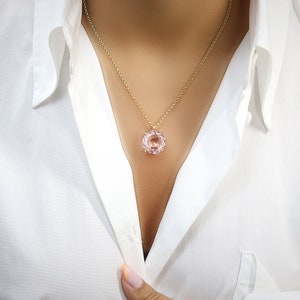 May include: A delicate gold chain necklace with a large, round, light pink gemstone pendant.