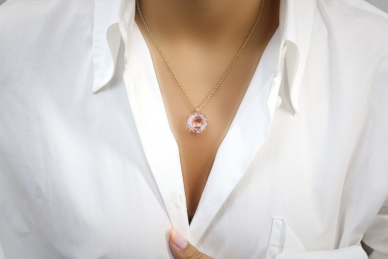May include: A delicate gold chain necklace with a large, round, light pink gemstone pendant.