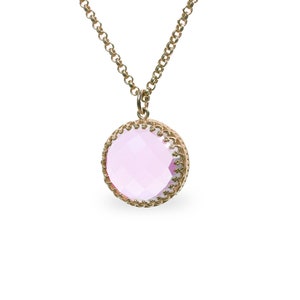 Op de afbeelding: Een gouden ketting met een roze edelsteen hanger. De hanger is rond en heeft een decoratieve gouden rand.