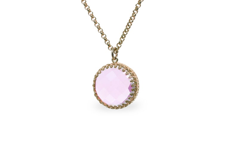 Op de afbeelding: Een gouden ketting met een roze edelsteen hanger. De hanger is rond en heeft een decoratieve gouden rand.