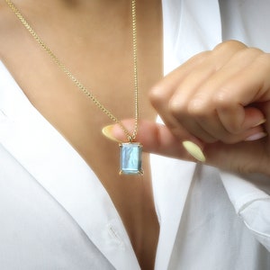 May include: A gold chain necklace with a rectangular pendant featuring a blue and gray gemstone.
