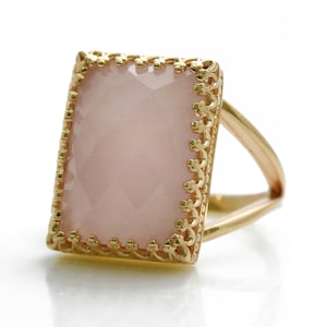 May include: A gold ring with a delicate, ornate design featuring a rectangular pink gemstone.