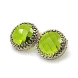 May include: A pair of green gemstone earrings with silver settings. The earrings have a round, faceted design and a decorative border.