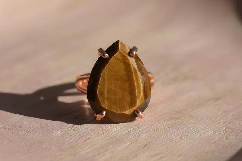 A close-up image of a large, irregularly shaped gemstone, possibly a diamond or a tiger's eye, set in a ring with a metal band.