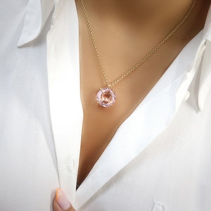 May include: A delicate gold chain necklace with a round, light pink gemstone pendant.