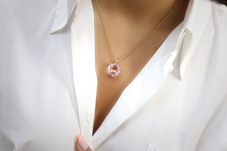 May include: A delicate gold chain necklace with a round, light pink gemstone pendant.