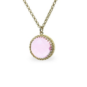 Op de afbeelding: Een gouden ketting met een roze edelsteen hanger. De hanger is rond en heeft een delicaat gouden filigraan ontwerp.