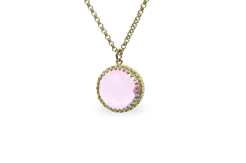 Op de afbeelding: Een gouden ketting met een roze edelsteen hanger. De hanger is rond en heeft een delicaat gouden filigraan ontwerp.