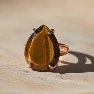 A large, oval-shaped amber-colored gemstone, possibly a tiger eye, is displayed on a wooden surface.
