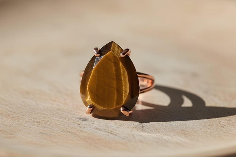 A large, oval-shaped amber-colored gemstone, possibly a tiger eye, is displayed on a wooden surface.