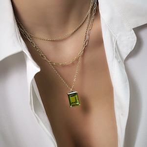 Pode incluir: Um colar de corrente de ouro com três fios e um pingente com uma grande pedra verde esmeralda retangular.