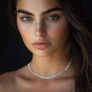 May include: A silver curb chain necklace with a classic design. The necklace is worn by a person with long brown hair and light skin.