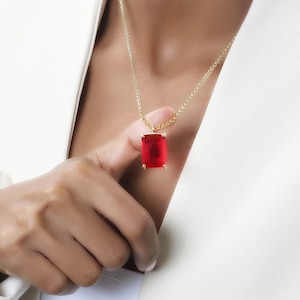 Puede incluir: Un collar de cadena dorada con un colgante de piedra preciosa roja rectangular grande.