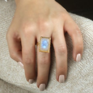 Puede incluir: Un anillo de oro con una piedra de luna rectangular engastada en un marco decorativo.