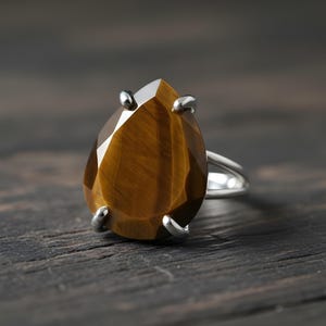 A close-up image of a ring with a large, irregularly shaped gemstone, likely a diamond, set in a silver band.
