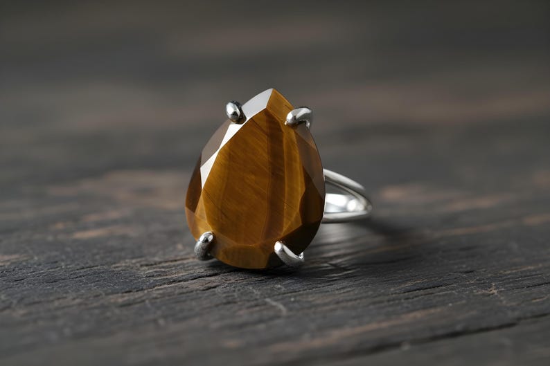 A close-up image of a ring with a large, irregularly shaped gemstone, likely a diamond, set in a silver band.