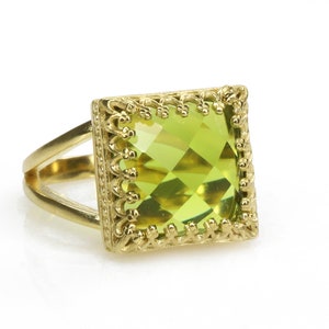 Puede incluir: Un anillo de oro con una piedra preciosa verde cuadrada engastada en un marco de oro decorativo.