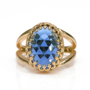 K&ouml;nnte beinhalten: Ein goldener Ring mit einem blauen, ovalen Edelstein, der in einem dekorativen Goldrahmen gefasst ist.