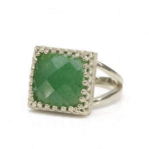 Puede incluir: Anillo de plata con una piedra preciosa verde cuadrada y facetada. La piedra preciosa est&aacute; engastada en un marco calado decorativo. El anillo tiene un dise&ntilde;o de ca&ntilde;a dividida, a&ntilde;adiendo un toque moderno a la joya.