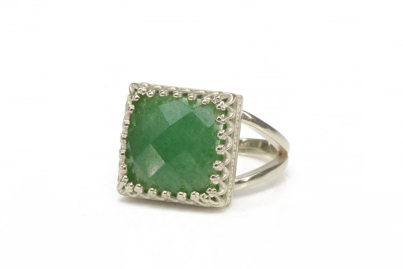 Puede incluir: Anillo de plata con una piedra preciosa verde cuadrada y facetada. La piedra preciosa est&aacute; engastada en un marco calado decorativo. El anillo tiene un dise&ntilde;o de ca&ntilde;a dividida, a&ntilde;adiendo un toque moderno a la joya.