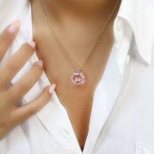 May include: A delicate gold chain necklace with a pink gemstone pendant. The pendant is round and has a faceted design.
