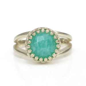 May include: A silver ring with a green gemstone set in a decorative silver bezel. The ring has a double band.