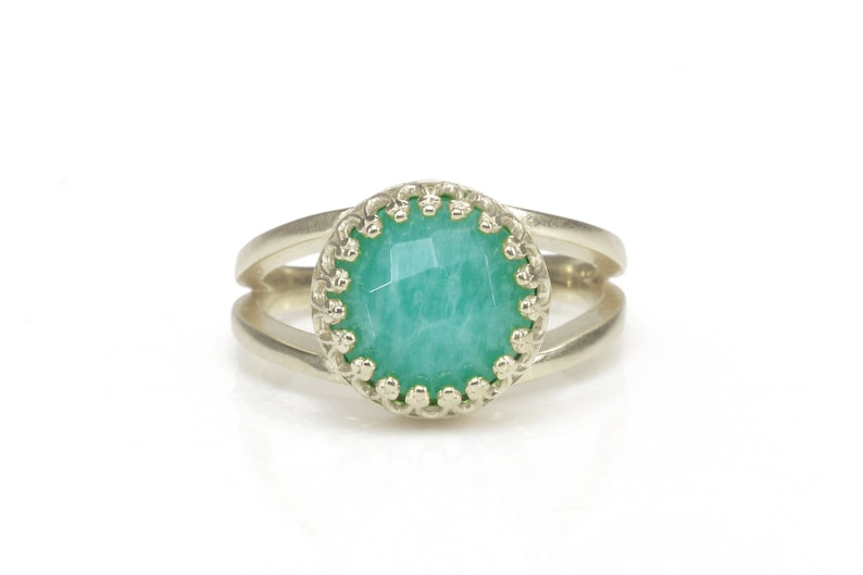 May include: A silver ring with a green gemstone set in a decorative silver bezel. The ring has a double band.