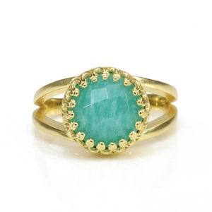 May include: A gold ring featuring a green gemstone set within an ornate gold bezel. The ring has a split shank design.