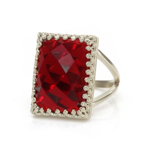 Peut inclure: Une bague en argent avec une grande pierre précieuse rouge facetée sertie dans un cadre décoratif en argent.