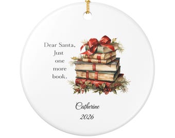 May include: A round white ceramic ornament featuring a stack of books tied with a red ribbon and holly, with the text Dear Santa, Just one more book. The ornament is personalized with the name Catherine and the year 2026, hanging from a gold cord.
