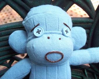 May include: A blue sock monkey with brown eyes and a brown mouth. The monkey is wearing a blue hat and has two blue buttons for eyes.