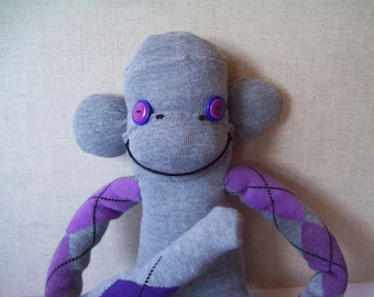 May include: A gray sock monkey with purple and gray argyle patterned arms and legs. The monkey has black eyes with purple buttons and a black stitched smile.
