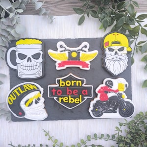 Peut inclure: Un ensemble de six biscuits décorés représentant une chope de bière en forme de crâne, un emblème de moto ailé avec le texte HAPPY BIRTHDAY, un crâne barbu avec une casquette jaune, un crâne avec un casque OUTLAW, un écusson born to be a rebel et un motard.