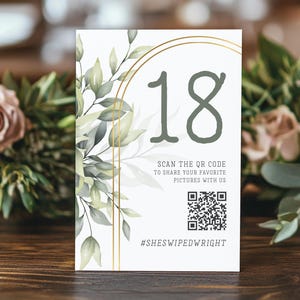 May include: A white table number card with the number 18 in green, surrounded by gold arches and green foliage. The card includes a QR code and the text "SCAN THE QR CODE TO SHARE YOUR FAVORITE PICTURES WITH US" and the hashtag "#SHESWIPEDWRIGHT".