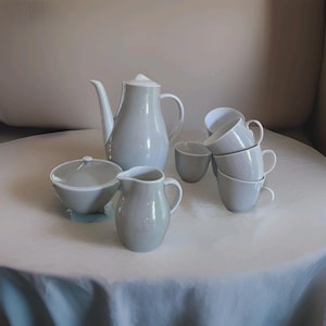 May include: A light gray ceramic tea set consisting of a tall teapot with a lid, a lidded sugar bowl, a small creamer pitcher, and four matching tea cups. Each piece features a smooth, solid-colored finish and a simple, functional design.