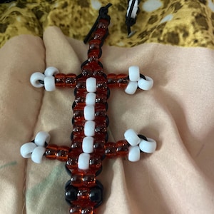May include: A beaded lizard figurine in red and white, with black accents. The lizard's body is primarily red, with white beads forming a pattern down the center. The legs and tail are also red and white. The eyes are black.