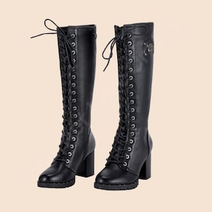 May include: A pair of black knee-high boots with a lace-up design. The boots have a block heel and a decorative emblem on the side. The boots are made of a smooth material and have a round toe.