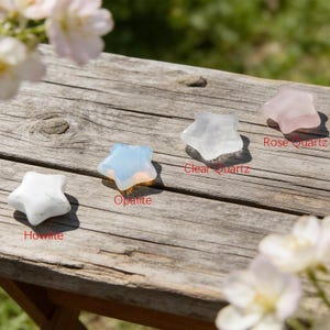 May include: A collection of star-shaped gemstones, including Howlite, Opalite, Clear Quartz, and Rose Quartz, are displayed on a weathered wooden surface. The gemstones vary in color from white to translucent, with the Opalite exhibiting a blue-white iridescence. The names of the stones are labeled.
