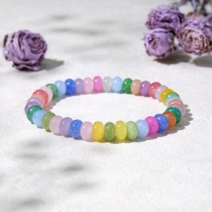May include: A colorful beaded bracelet featuring a rainbow of pastel colors. The bracelet is made of small, round beads in shades of pink, blue, green, yellow, and purple. The bracelet is displayed on a white surface.