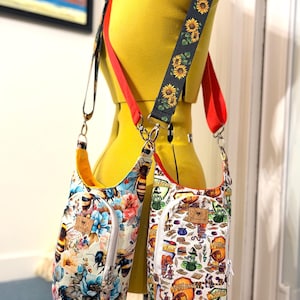 May include: Two water bottle bags with adjustable straps. One bag features a floral and bee pattern, the other has a pattern of books, potions, and crests. The straps are red and black with a sunflower design.